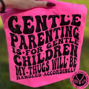Puede incluir: Un artículo de tela rosa brillante con las palabras "GENTLE PARENTING IS FOR GENTLE CHILDREN MY THUGS WILL BE HANDLED ACCORDINGLY" en negro, con letras estilizadas. El artículo se muestra sobre un fondo verde.