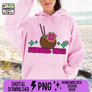 May include: Pink hoodie featuring a graphic of a coconut with a flower and two straws. The graphic is surrounded by green stars and the text "SUMMER VIBES" in pink letters.