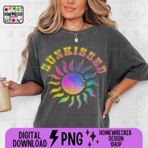 Puede incluir: Una camiseta gris oscura con un gráfico de sol arcoíris y el texto "SUNKISSED" en una fuente retro.
