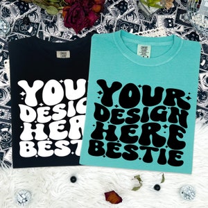 May include: Two t-shirts with the text "Your design here bestie" in a retro font. One t-shirt is black with white text and the other is teal with black text.