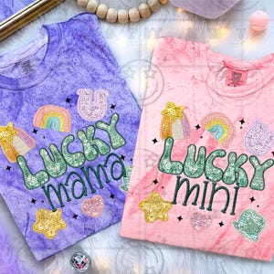 May include: Two tie-dye t-shirts, one purple and one pink, with embroidered designs. The purple shirt says "LUCKY mama" and the pink shirt says "LUCKY mini". Both shirts feature rainbows, stars, and shamrocks.