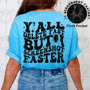 May include: A light blue t-shirt with the text "Y'ALL DELETE FAST BUT! SCREENSHOT FASTER" in black, retro-style lettering. A small graphic of a phone taking a photo is on the front pocket. The shirt has rolled-up sleeves.