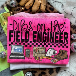 Może przedstawiać: Jasnoróżowa koszulka z czarnym napisem "Dibs on the FIELD ENGINEER". Projekt zawiera ilustracje narzędzi inżynieryjnych, laptopa, kasku, butów roboczych i rękawic.