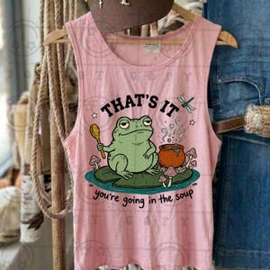 Op de afbeelding: Roze tanktop met een grillige kikkerprint. Het ontwerp toont een groene kikker met een lepel, een pan soep en de tekst "THAT'S IT you're going in the soup". De tanktop is mouwloos en gemaakt van een zachte stof.