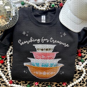 May include: Black sweatshirt with the text "Searching for treasure" and a stack of four vintage-style mixing bowls with floral patterns in shades of brown, pink, blue, and orange.