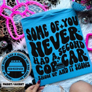以下が含まれることがあります： レトロなフォントで「Some of you never had a second cop car show up and it shows」と書かれた青いTシャツ。テキストは黒で、シャツは薄い青色です。シャツには、白黒の警察車の画像が描かれた小さなポケットが付いています。