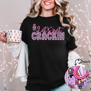 May include: Black t-shirt with a pink and purple design that says "Let's get crackin'" with a nutcracker illustration.
