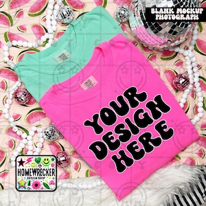 May include: Two blank t-shirts, one pink and one teal, are laid out on a watermelon print background. The pink t-shirt has the text "YOUR DESIGN HERE" in black, retro-style lettering.