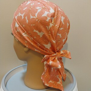 May include: A white and orange bandana with a leaf pattern. The bandana is tied around a mannequin's head.
