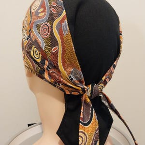 May include: A black and brown patterned bandana with a black fabric backing. The bandana is tied in a knot at the back of the head.