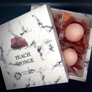 May include: Two peach-coloured makeup sponges in a white marble-patterned box with the text "CB Makeup Beauty Peach Sponge Premium latex free makeup sponge".