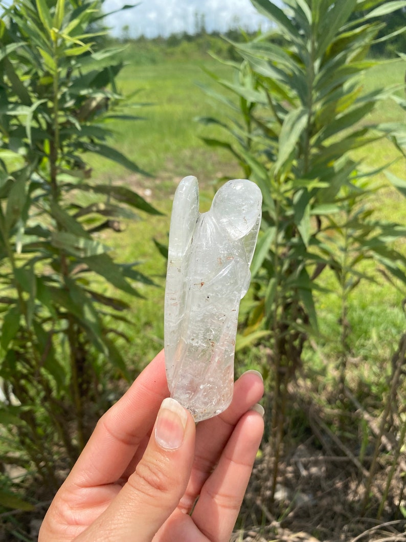 Peut inclure: Un cristal de quartz clair sculpt&eacute; en forme d'ange. L'ange a des ailes et une longue robe flottante. Le cristal est translucide et a un l&eacute;ger &eacute;clat.
