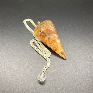 May include: A clear quartz crystal pendulum with a silver chain. The crystal is filled with small, colorful stones, including red, orange, and yellow.