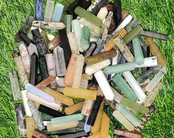 May include: A collection of colorful, polished, pointed gemstone wands. The wands are made of various types of stones, including green, blue, brown, and white. The wands are arranged in a pile, with some of them overlapping.