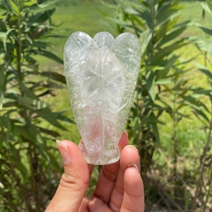 Peut inclure: Un cristal de quartz clair sculpt&eacute; en forme d'ange. L'ange a des ailes et un corps, et se tient debout.