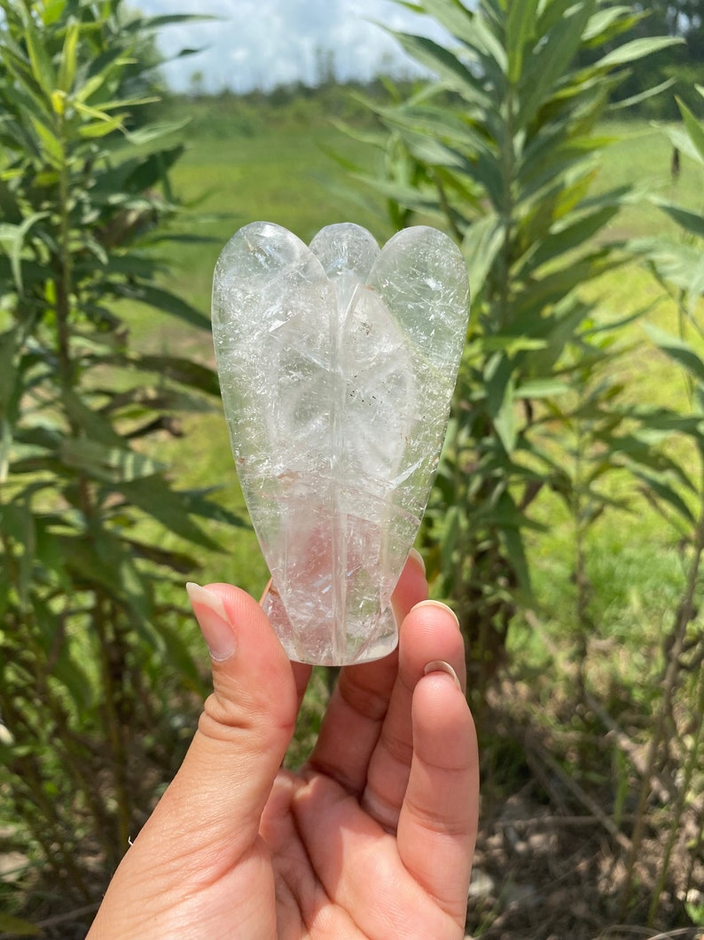 Peut inclure: Un cristal de quartz clair sculpt&eacute; en forme d'ange. L'ange a des ailes et un corps, et se tient debout.