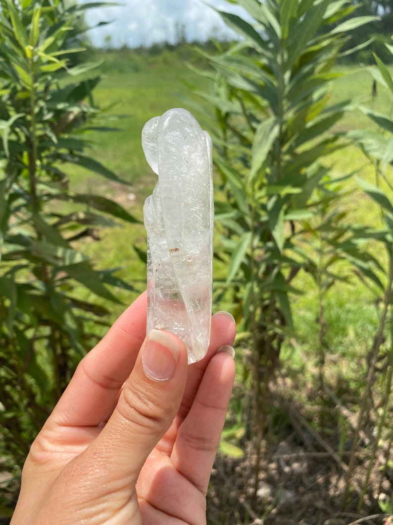 Peut inclure: Un cristal de quartz clair sculpt&eacute; en forme de deux figures qui s'embrassent. Le cristal est lisse et poli, avec des inclusions internes visibles.
