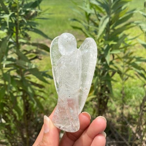 Peut inclure: Une figurine d'ange en cristal de quartz clair, sculpt&eacute;e dans une seule pi&egrave;ce de cristal. L'ange a un design d&eacute;taill&eacute; avec des ailes et une robe fluide.