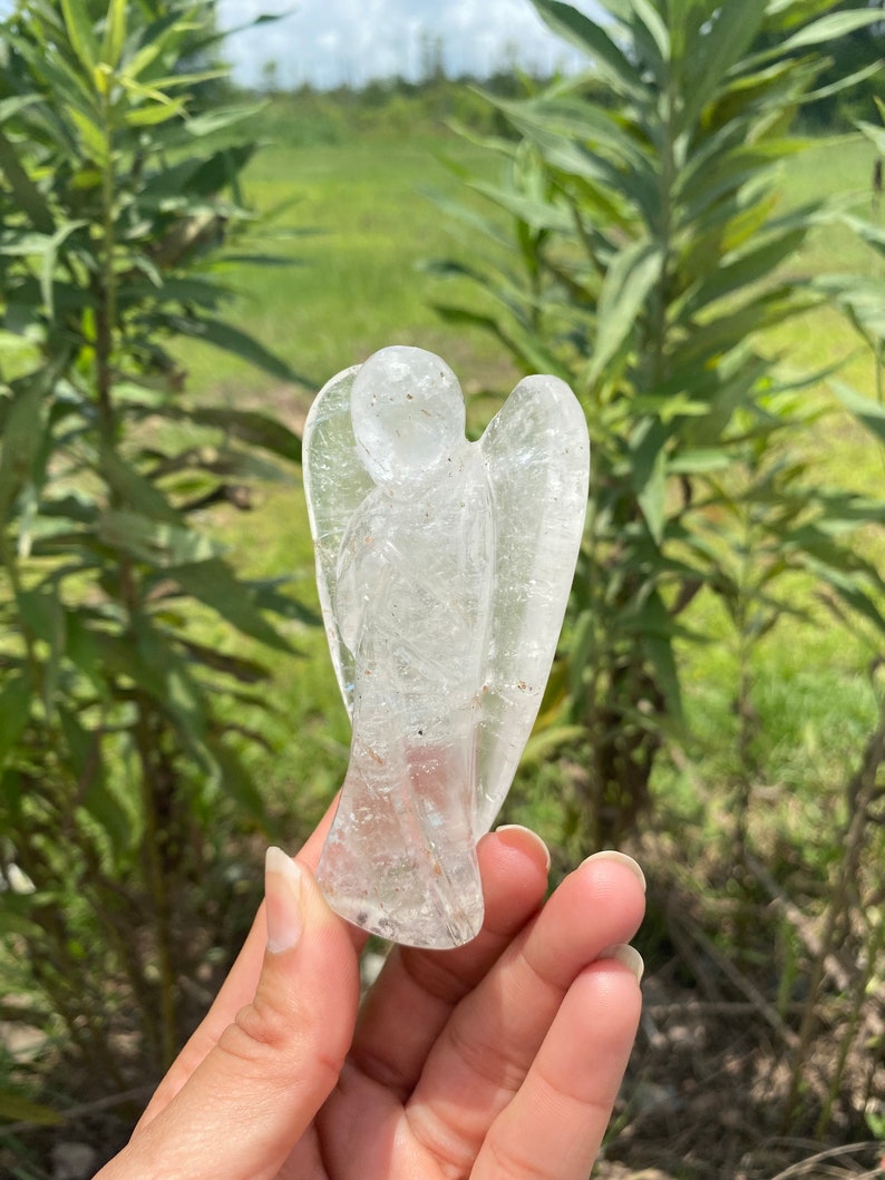 Peut inclure: Une figurine d'ange en cristal de quartz clair, sculpt&eacute;e dans une seule pi&egrave;ce de cristal. L'ange a un design d&eacute;taill&eacute; avec des ailes et une robe fluide.