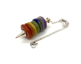 May include: A silver chain pendulum with a pointed tip and seven stacked chakra stones. The stones are red, orange, yellow, green, blue, indigo, and violet.