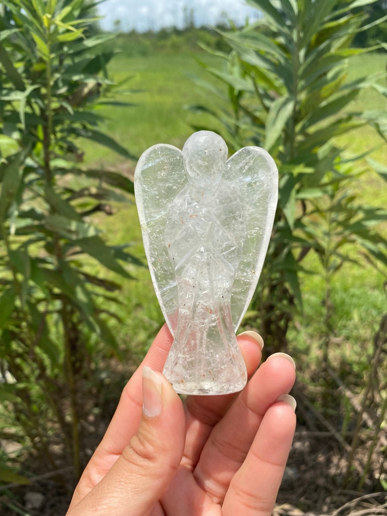 Peut inclure: Une figurine d'ange en quartz clair avec une sculpture d&eacute;taill&eacute;e. L'ange est debout, les ailes d&eacute;ploy&eacute;es et les mains jointes en pri&egrave;re. La figurine est faite de cristal de quartz naturel et a une apparence translucide.