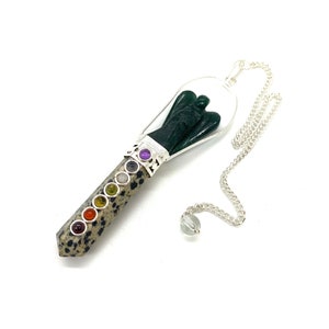 May include: A green angel shaped pendulum with a silver chain and a clear crystal at the end. The pendulum is made of a speckled stone with seven colored stones representing the chakras.