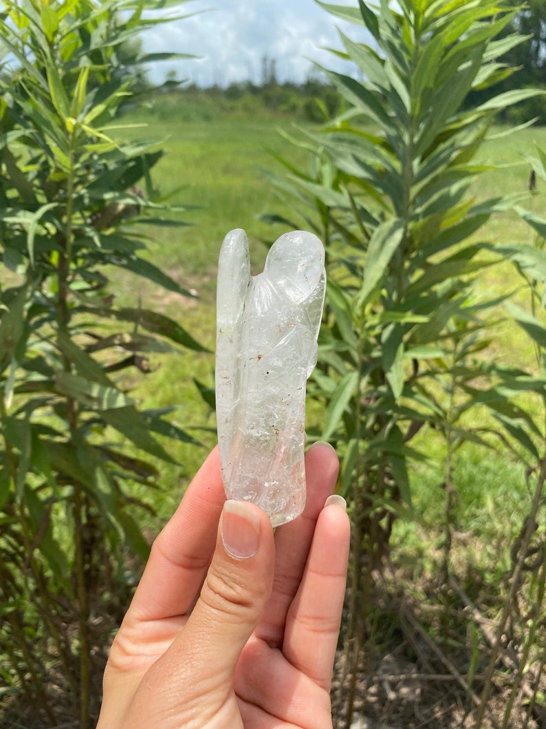 Peut inclure: Une figurine d'ange en cristal transparent avec une texture brute et naturelle. L'ange est debout, les ailes d&eacute;ploy&eacute;es.