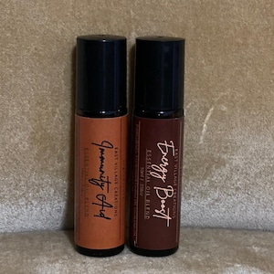 Puede incluir: Dos botellas de 10 ml de mezcla de aceites esenciales en roll-on. Una botella es marrón con el texto "Energy Boost" y la otra es naranja con el texto "Immunity Aid". Ambas botellas están etiquetadas con "East Village Creations".