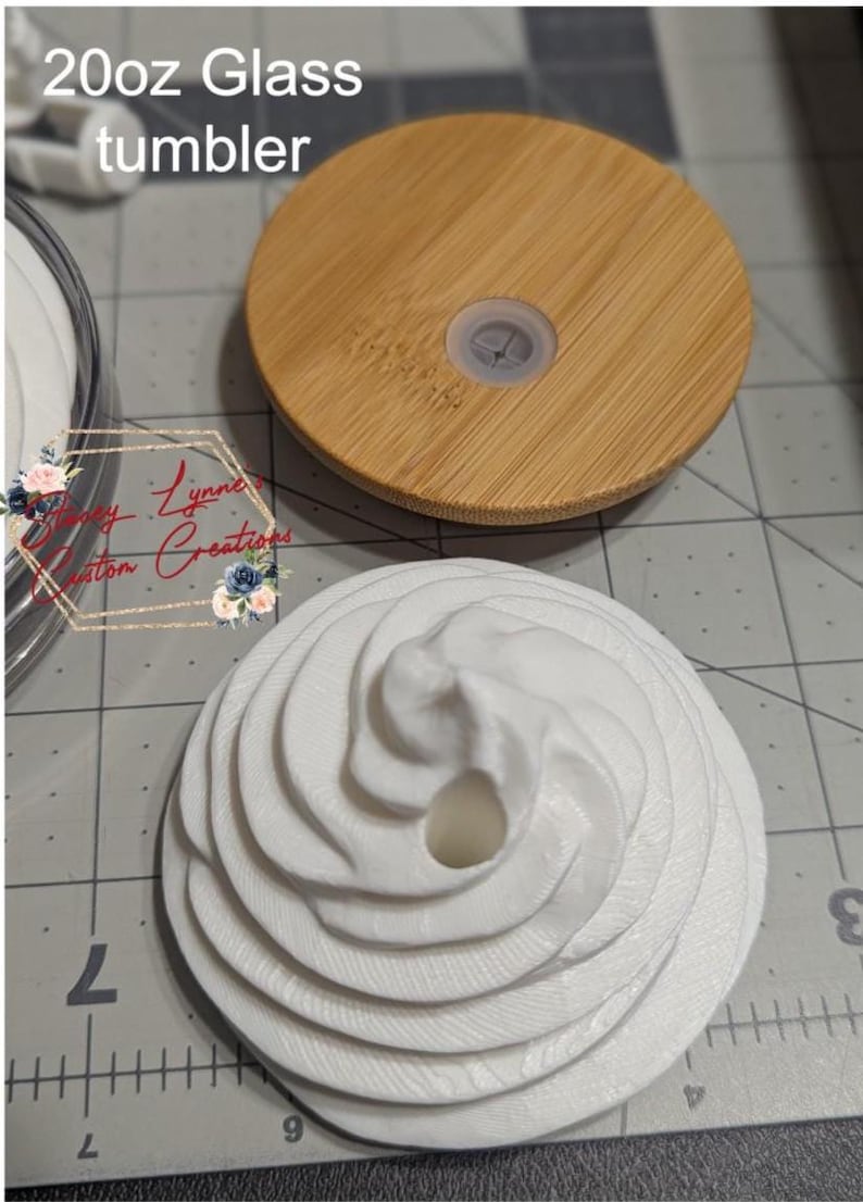 May include: A 20oz glass tumbler with a bamboo lid and a white, textured, decorative top. The bamboo lid is round with a clear plastic stopper. The white top has a spiral design. The text "20oz Glass tumbler" is visible.