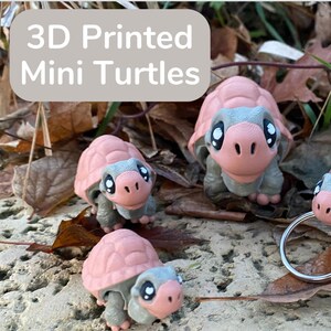 May include: A collection of 3D-printed mini turtles in various poses. Each turtle has a pink shell, gray body, and large, expressive eyes. Some turtles have key rings attached. The image includes the text "3D Printed Mini Turtles" and "HOME OF THE BEST 3D PRINTED THINGS."