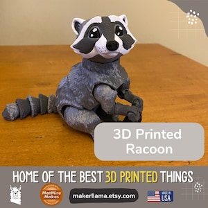 May include: 3D printed raccoon figurine with a gray and white fur pattern. The raccoon is sitting with its tail curled behind it. The figurine is on a wooden surface. The text "3D Printed Raccoon" is on a gray background.