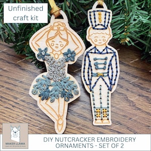 May include: Unfinished craft kit featuring two wooden DIY Nutcracker embroidery ornaments. One ornament is a ballerina with blue and gray embroidery, the other is a soldier with blue and gold embroidery. The text "DIY NUTCRACKER EMBROIDERY ORNAMENTS - SET OF 2" is visible.