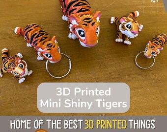 May include: Five 3D printed miniature tiger figurines. The tigers are orange and black with shiny paint. The tigers are on a wooden surface. The text "3D Printed Mini Shiny Tigers" is on a gray background. The text "HOME OF THE BEST 3D PRINTED THINGS" is on a white background. The text "makerllama.etsy.com" is on a white background. The text "MADE IN USA" is on a white background.