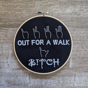 May include: Black embroidery hoop with white lettering that reads "OUT FOR A WALK BITCH" with four white hand gestures above the text.