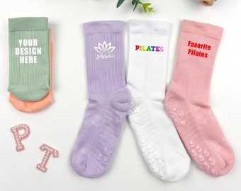 May include: Three pairs of socks with different designs. One pair is light green with the text "Your Design Here". Another pair is lavender with a white lotus flower and the text "Pilates". The last pair is pink with the text "Favorite Pilates".