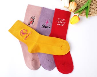 May include: A collection of colorful socks, including yellow, pink, purple, and red. The yellow sock has a logo and text, while the pink and purple socks feature embroidered designs and the word "Dance". The red sock has the text "YOUR DESIGN HERE".
