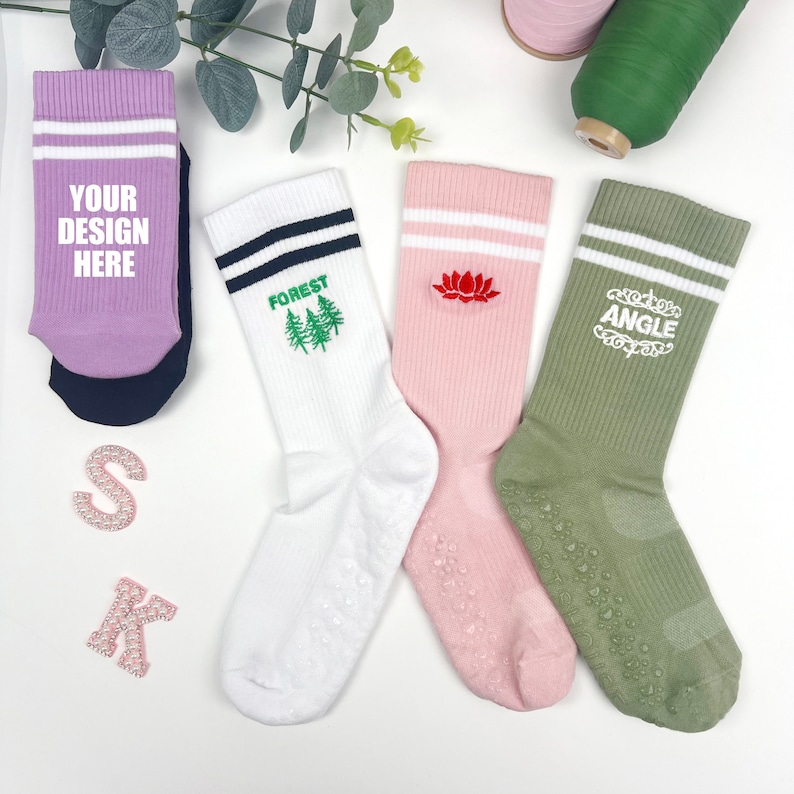 May include: Four pairs of white, pink, green and purple socks with colourful designs. The socks have white stripes and non-slip grips on the bottom. The designs include "Your Design Here", "Forest", a lotus flower and "Angle".