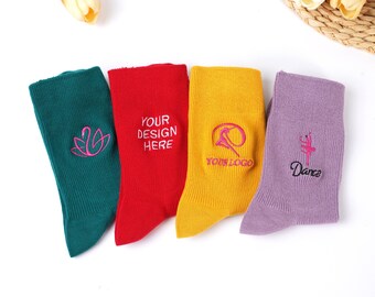 May include: Four pairs of colorful socks are displayed, each with a unique design. The socks are teal, red, yellow, and lavender. The teal sock has a pink swan design, the red sock has the text "YOUR DESIGN HERE", the yellow sock has a pink logo, and the lavender sock has a ballerina design with the word "Dance".