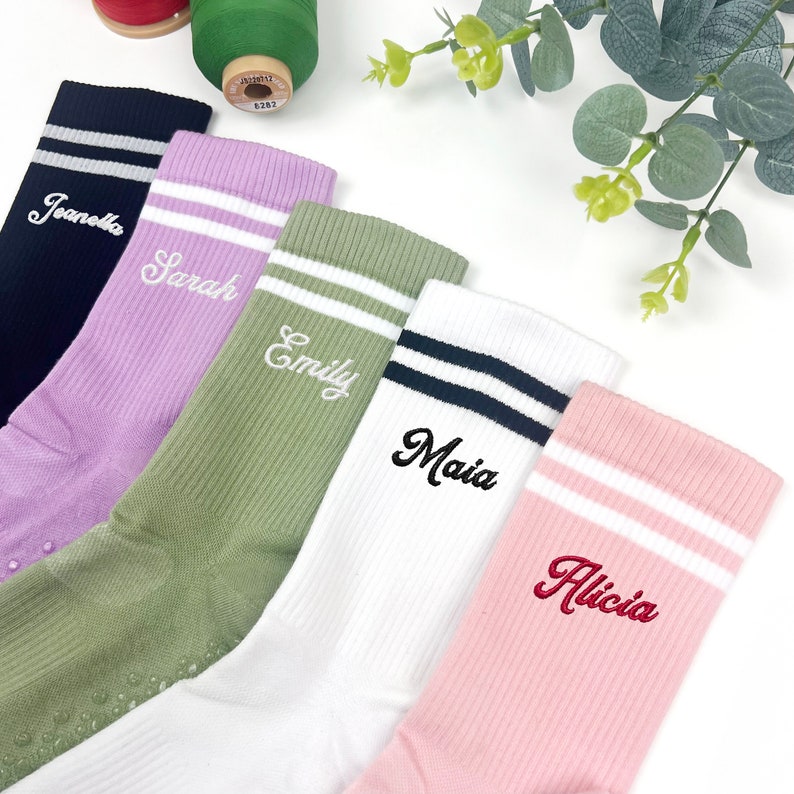 May include: Five pairs of colourful socks with white stripes and personalised names embroidered on them. The names are "Jeanette", "Sarah", "Emily", "Maia", and "Alicia".