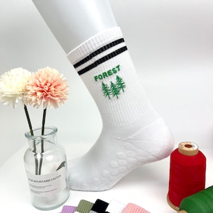 May include: White crew socks with black stripes and a green embroidered design of three pine trees with the word "FOREST" above them.