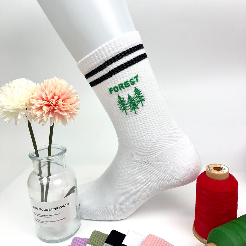 May include: White crew socks with black stripes and a green embroidered design of three pine trees with the word "FOREST" above them.