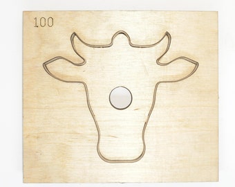 May include: A wooden die-cut template shaped like a cow's head with the number 100 printed on the top.
