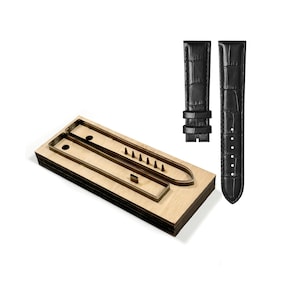 Peut inclure: Un bracelet de montre noir avec un motif crocodile et un gabarit de découpe en bois. Le gabarit est fait de bois en couches avec des découpes pour les composants du bracelet de montre. Le fond est blanc.