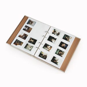 Peut inclure: Un album photo marron et blanc avec une couverture en plastique transparent et un classeur à anneaux. L'album est ouvert et rempli de photos Polaroid.