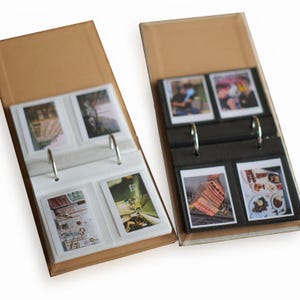 Peut inclure: Deux albums photos avec des couvertures en carton brun. Un album a des pages blanches et l'autre a des pages noires. Les deux albums ont des pochettes en plastique transparent pour contenir des photos. Les albums sont ouverts et montrent des photos de sujets variés.