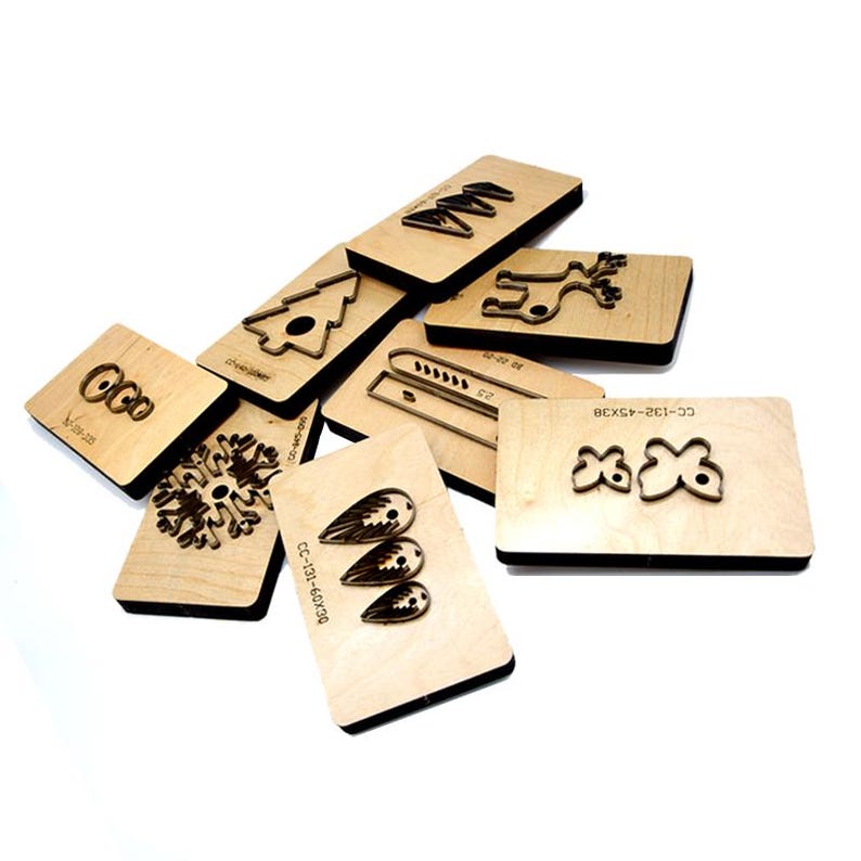 May include: A set of nine wooden craft dies featuring various Christmas-themed designs, including a snowflake, a reindeer, a Christmas tree, a bell, and a pair of wings. The dies are made of wood and have a natural finish.