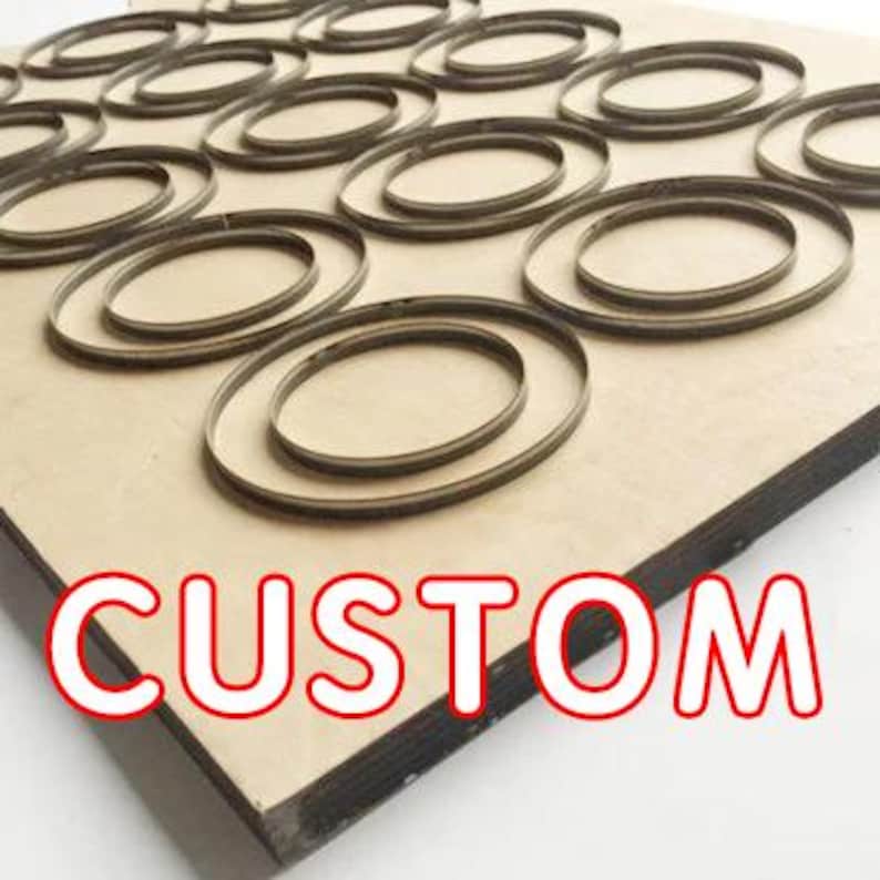 May include: A close-up of a wooden cutting die with multiple oval-shaped cutouts. The die is labeled "CUSTOM".