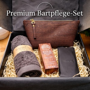 Könnte beinhalten: Schwarze Geschenkbox mit Bartpflegeprodukten. Enthält eine braune Reißverschlusstasche, ein gerolltes graues Waschhandtuch, eine Flasche Bartöl und ein schwarzes Lederetui. Die Box ist mit Stroh gefüllt.
