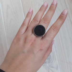 May include: A black ring with a textured circular design. The ring is made of metal and has a silver finish.