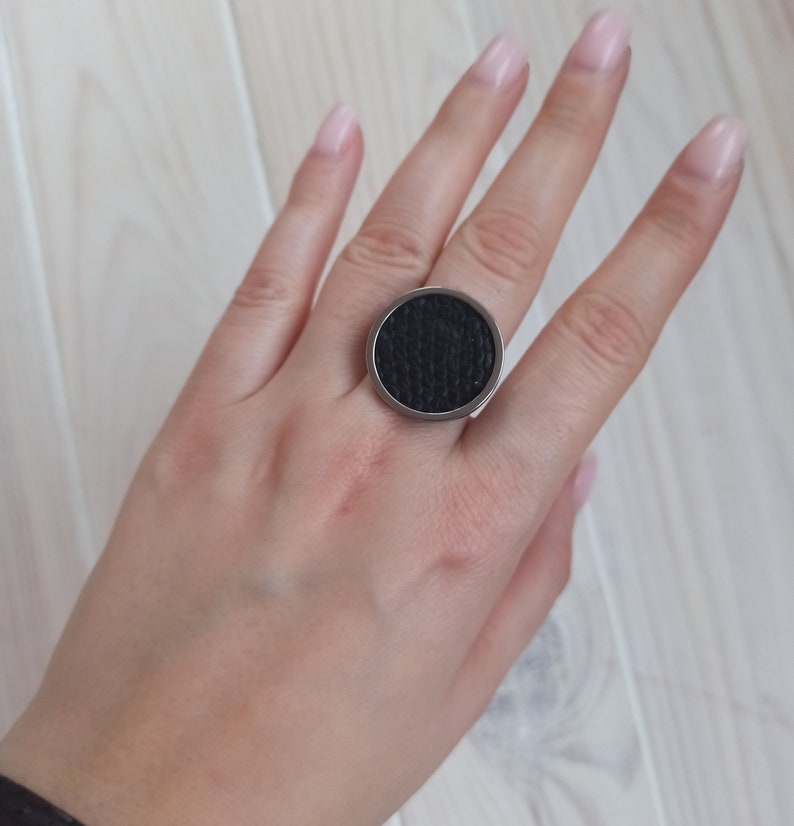 May include: A black ring with a textured circular design. The ring is made of metal and has a silver finish.
